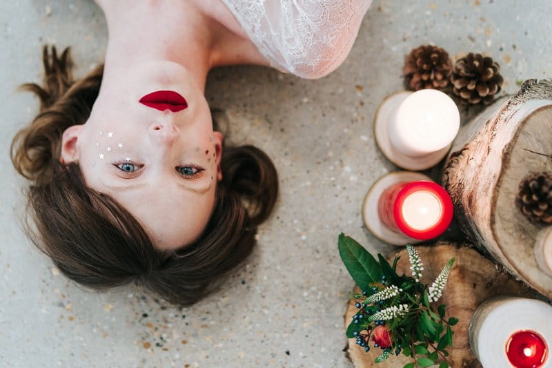 Bride lying down next to candles, logs and winter foliage