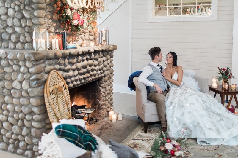 Bride and groom sitting next to fireplace