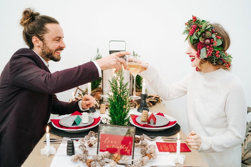 Bride and groom sitting at wedding table with red, green and black winter styling