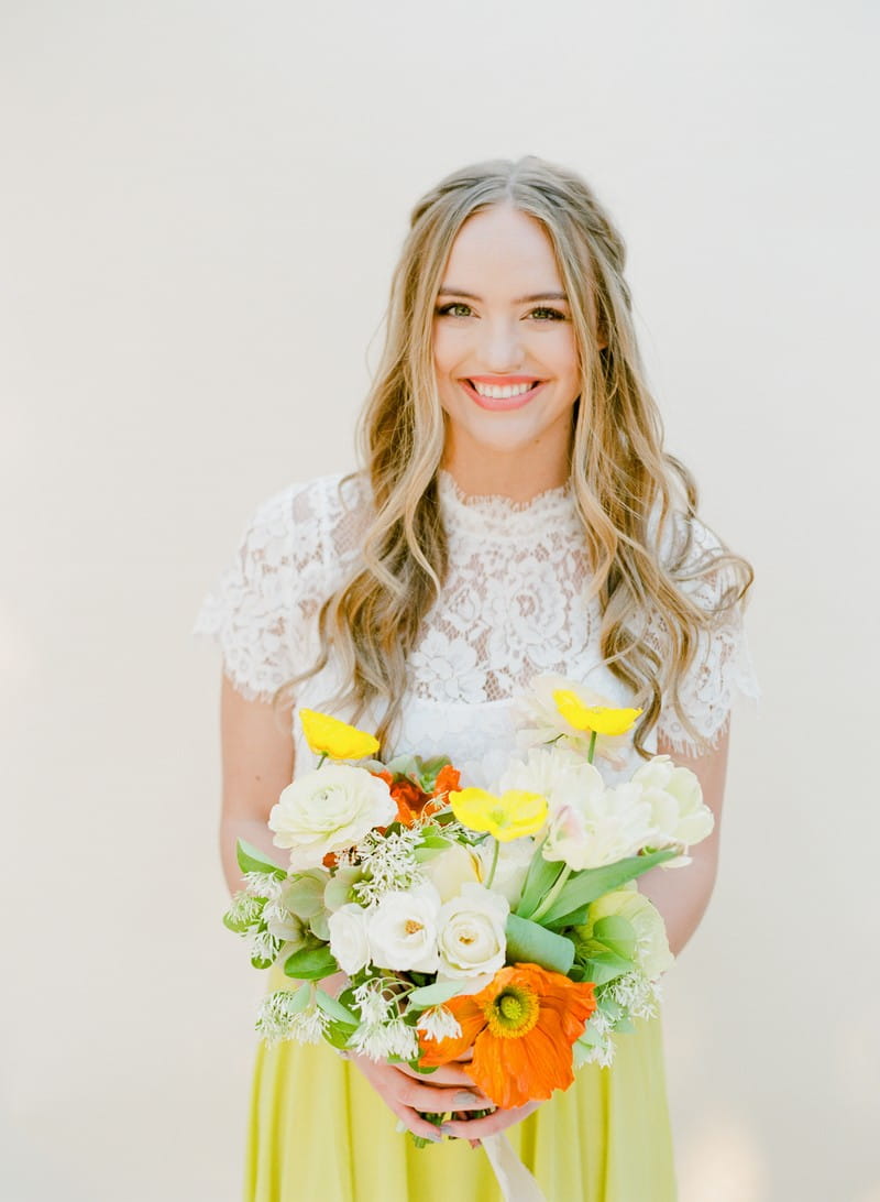 Bridesmaid with white lace top holding yellow, white and green bouquet