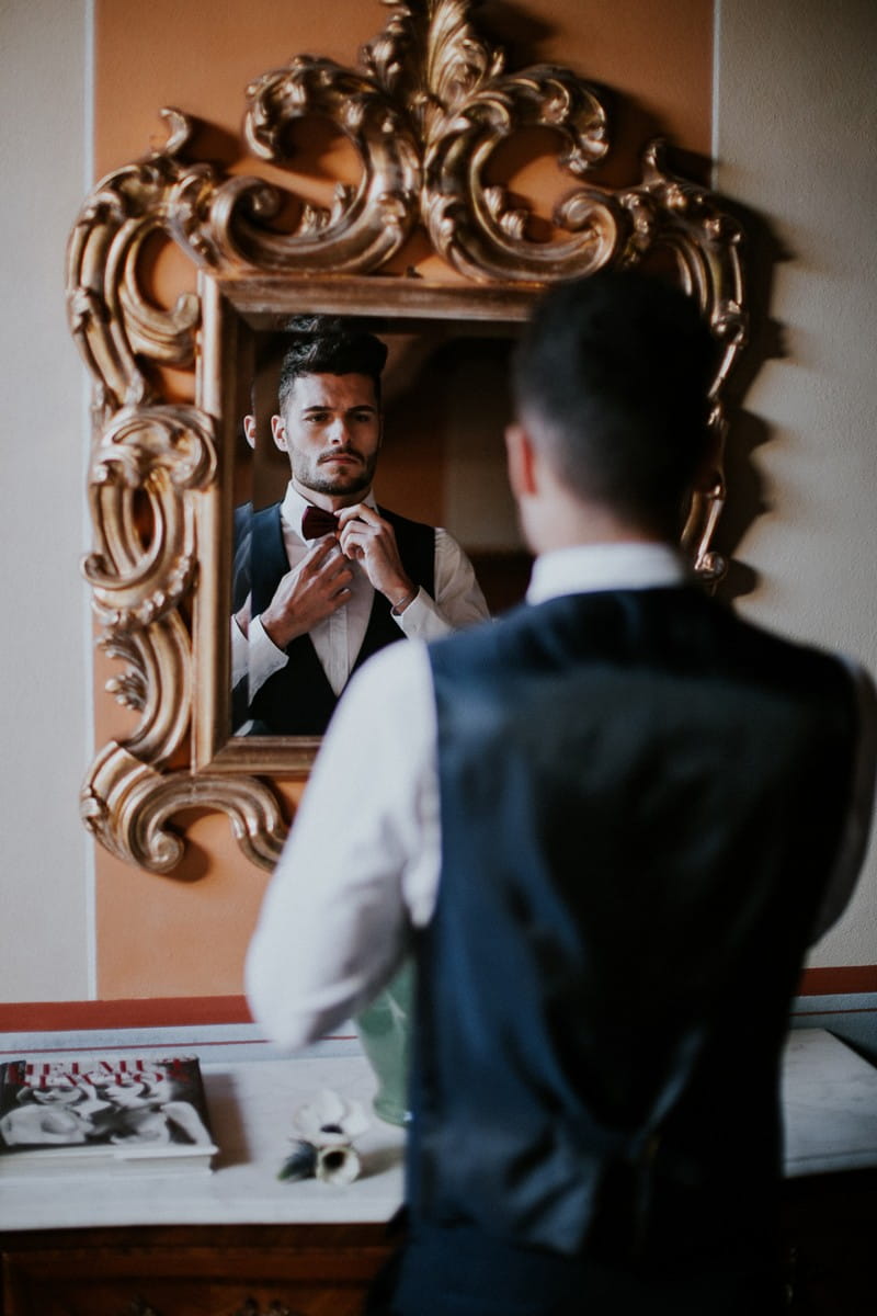 Groom doing bow tie in mirror