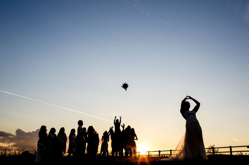 Silhouette of bride throwing bouquet to guests at sunset - Picture by Aaron Storry Photography