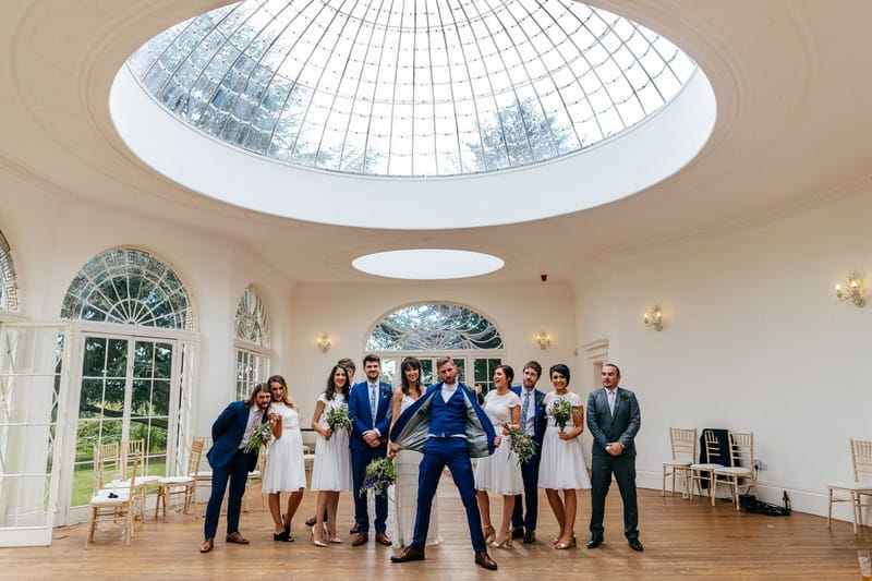 Groom standing in front of bridal party holding jacket out