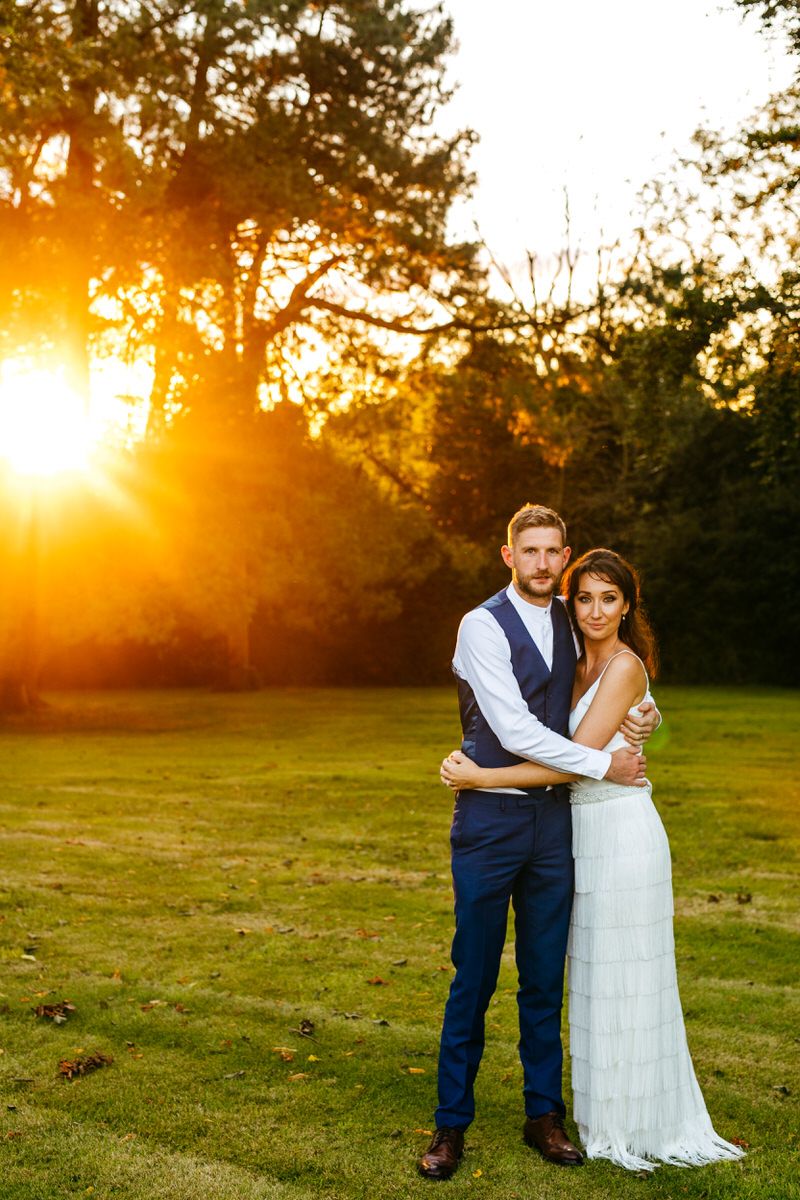 Bride and groom in grounds of Barton Hall with sun shining through trees