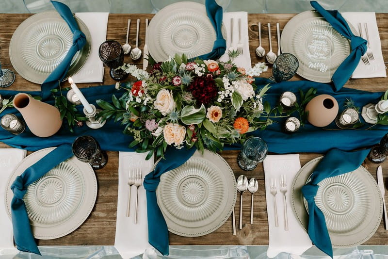 Winter wedding table with blue linen, glass plates and floral centrepiece