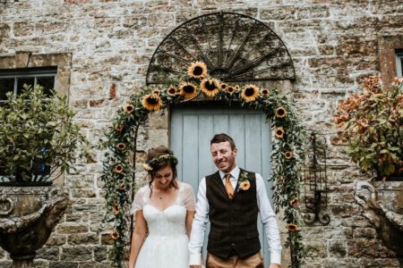 Bride and groom standing in front of sunflower arch - Picture by Ryan Goold Photography