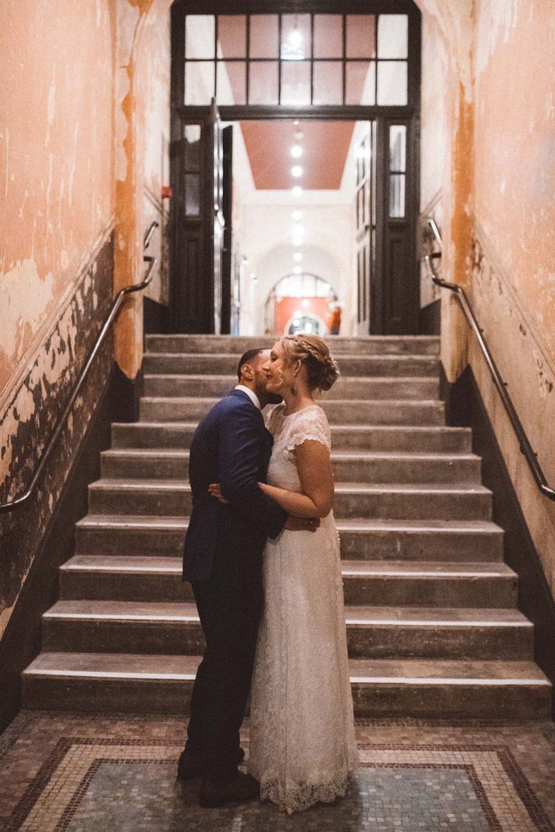 Groom kissing bride on the neck in corridor in front of steps - Picture by Barbara K. Photography