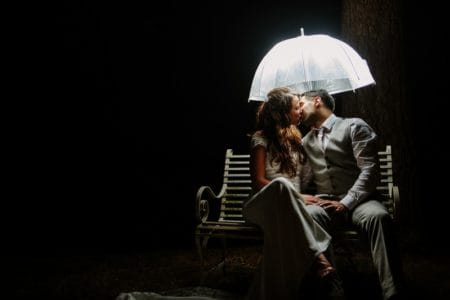 Bride and groom on bench kissing under lit umbrella in the dark - Picture by Nisha Haq Photography