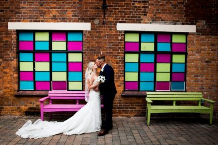 Bride and groom kissing between brightly coloued tiled windows - Picture by Nicola Norton Photography