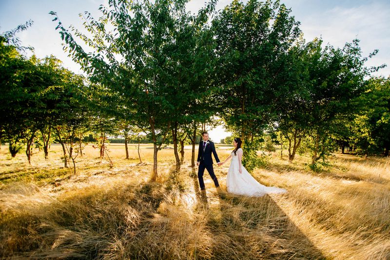 Bride and groom holding hands as they walk past trees - Picture by Ufniak Photography