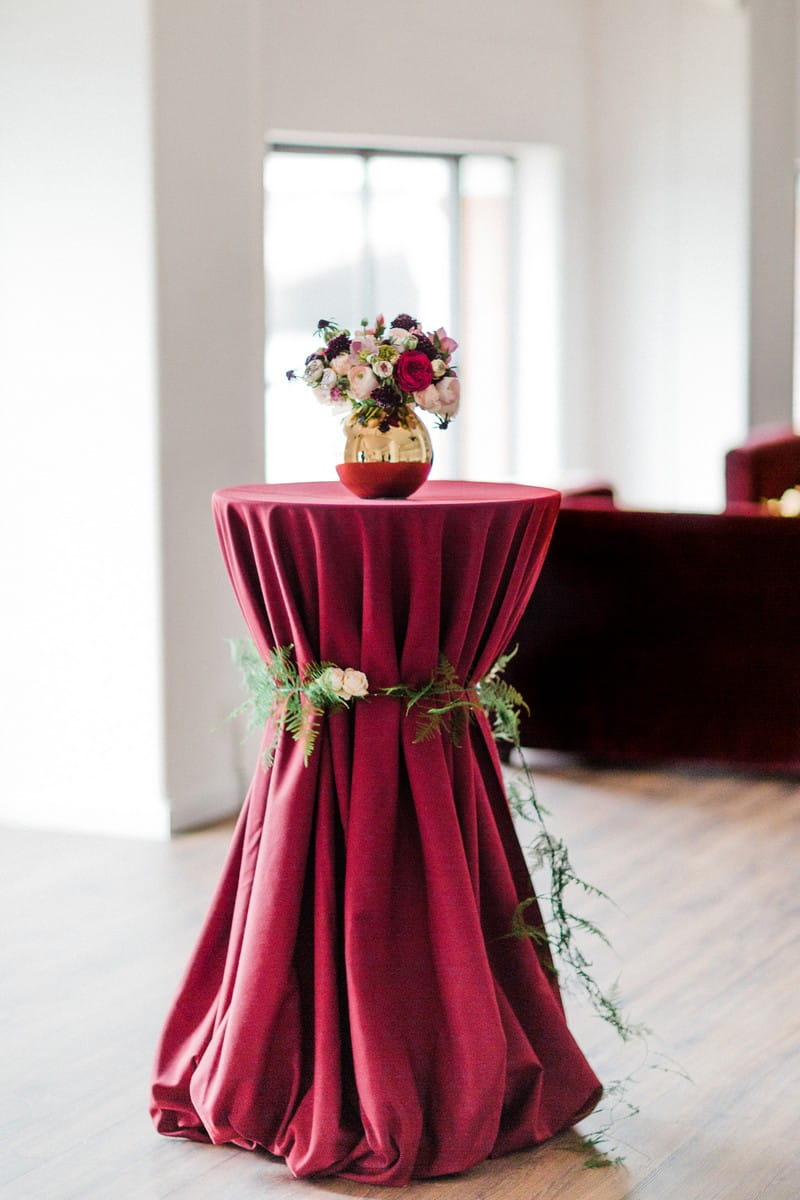 Vase of flowers on small table covered with red tablecloth and wrapped in foliage