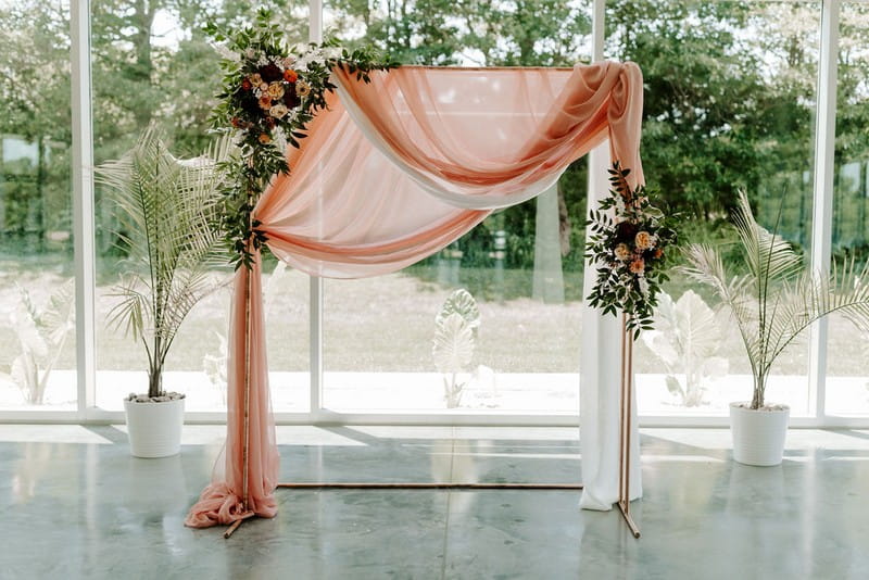 Wedding ceremony backdrop with pink fabric, foliage and flowers