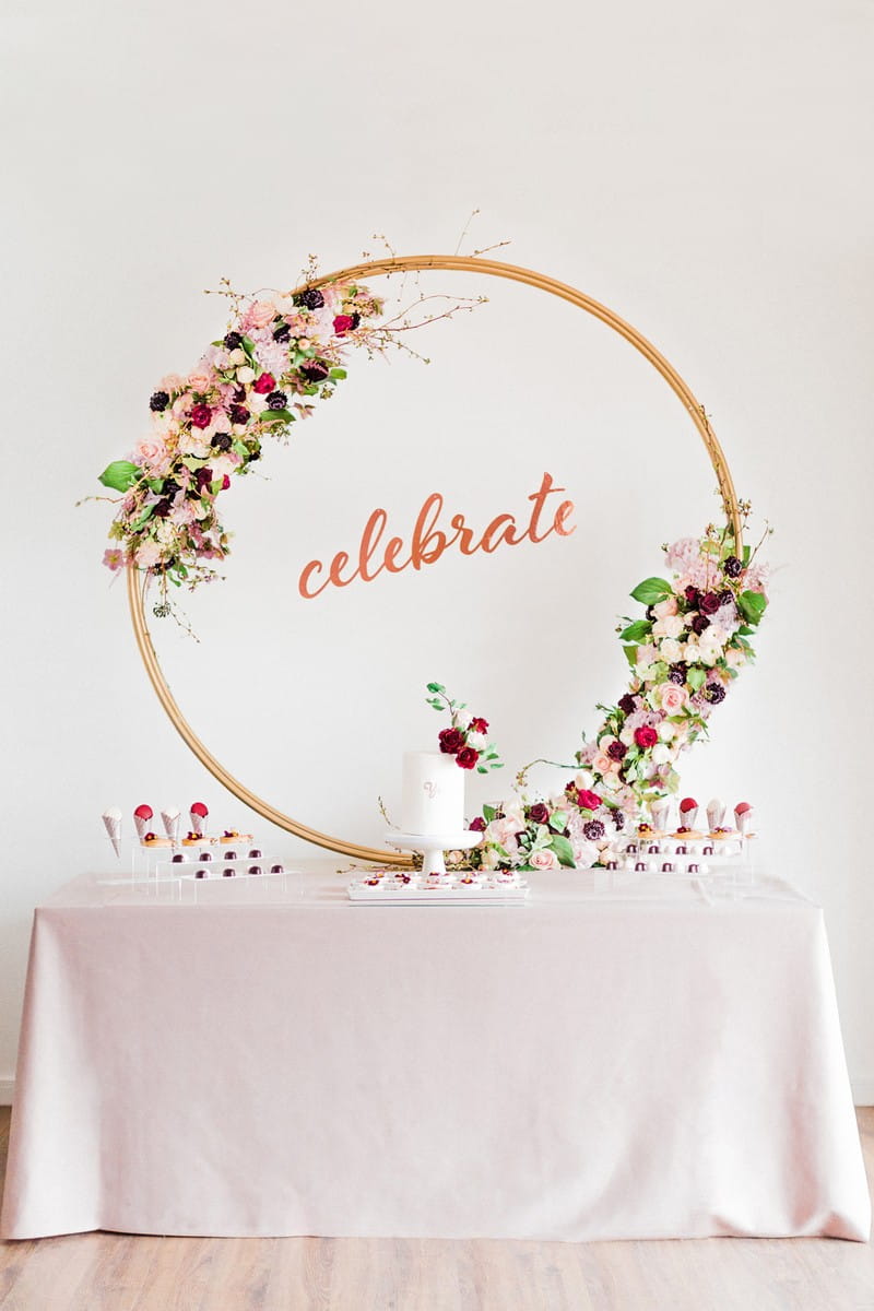 Dessert table for engagement party with large floral hoop and celebrate sign