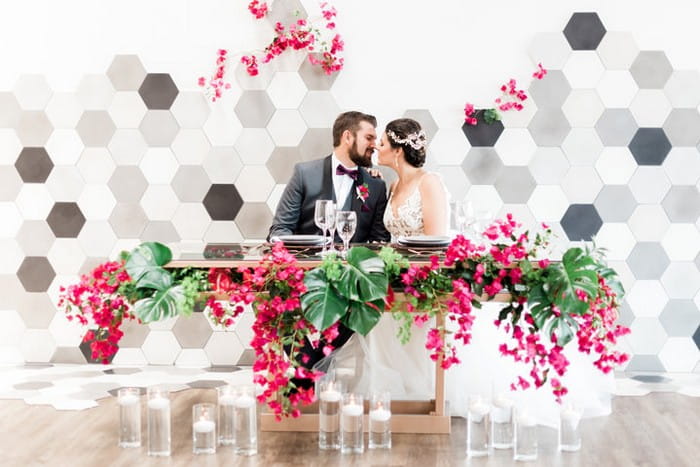 Bride and groom sitting at tropical wedding table styled with bougainvillea