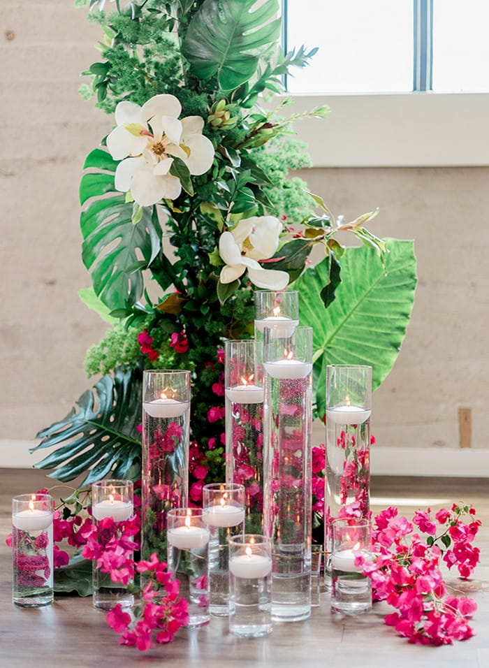 Vases of floating candles in front of tropical palm leaves and bougainvillea