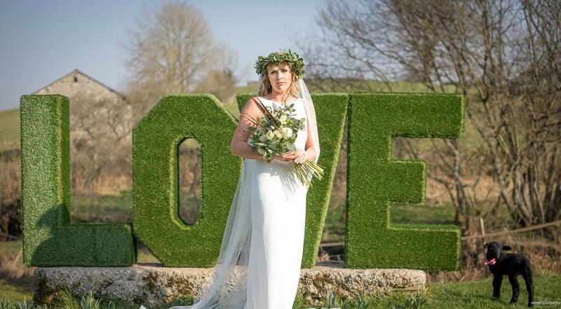 Bride standing in front of green hedge LOVE letters