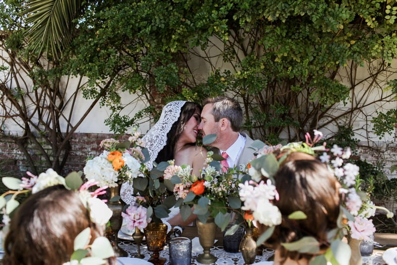 Bride and groom kissing behind wedding table flowers