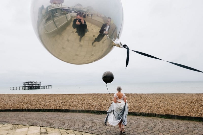 Refelection in balloon of photographer taking picture of bride carrying balloon across seafront - Picture by Kristian Leven Photography