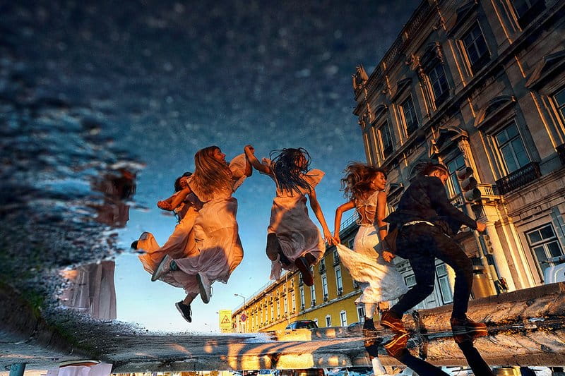 Reflection in puddle of bridesmaids jumping across road - Picture by Emin Kuliyev