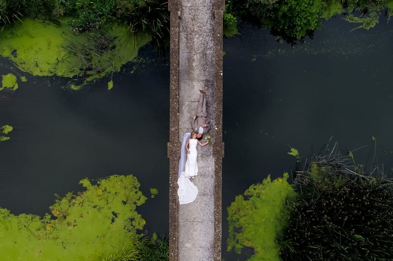 Aerial picture of bride and groom lying down on bridge - Picture by Copper and Blossom