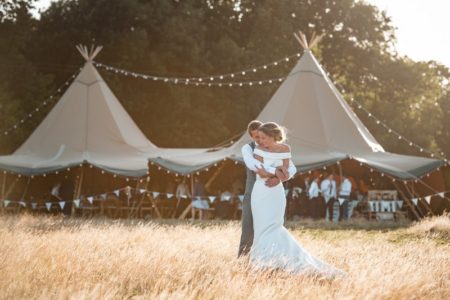 Groom hugging bride from behind in front of tipi - Picture by Penny Young Photography