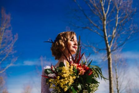 Bride holding bouquet in front of backdrop of blue sky and trees - Picture by Gina Fernandes Photography