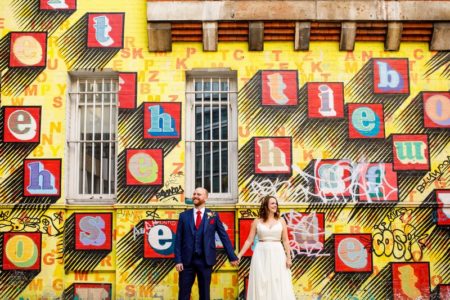 Bride and groom standing in front of wall with Ben Eine graffiti - Picture by John Woodward Photography