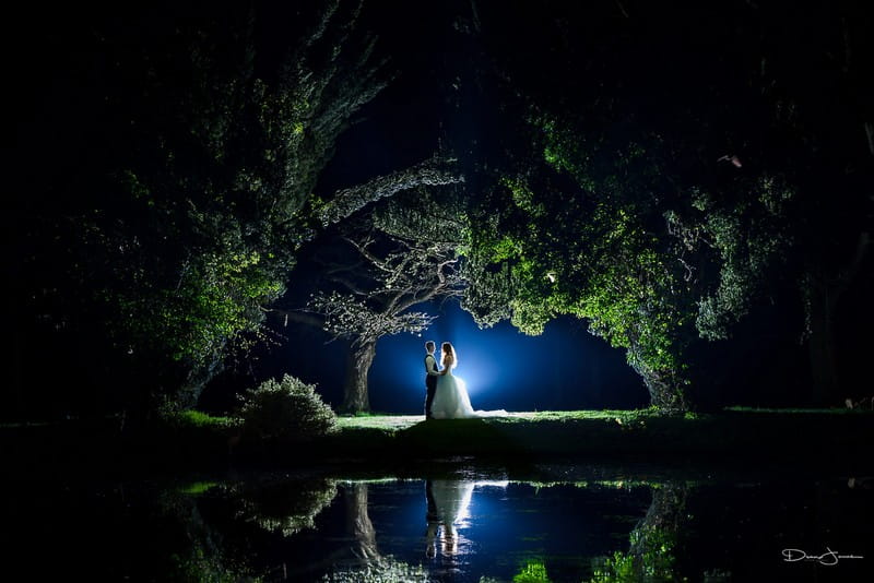 Bride and grom lit up under trees by lake in dark - Picture by Dean Jones Photography