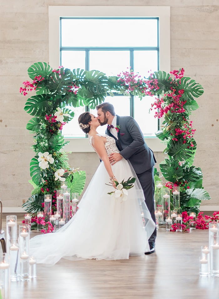 Bride and groom kissing in front of tropical wedding ceremony arch