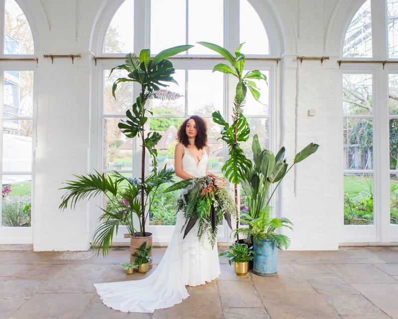 Bride standing in front of wedding arch styled with tropical foliage and leaves
