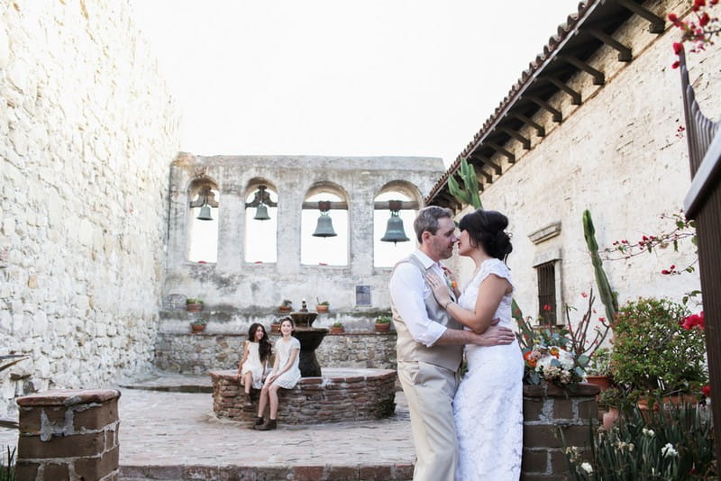 Bride, groom and flower girls in courtyard with fountain and bells