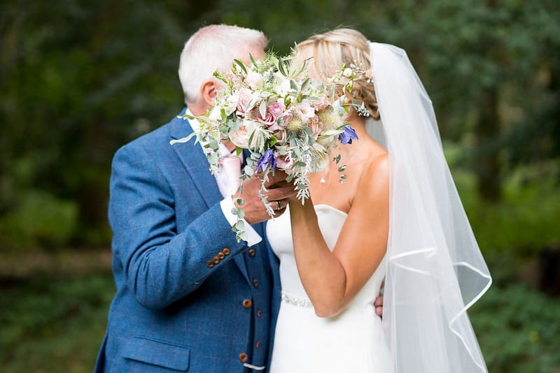 Bride and groom hiding faces behind bride's bouquet