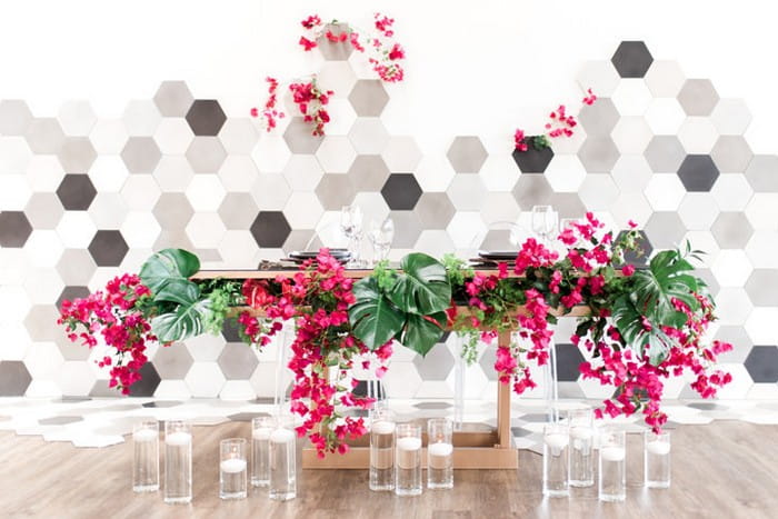 Wedding table styled with bougainvillea and palm leaves in front of hexagonal backdrop