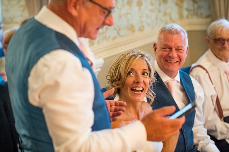 Bride smiling as man gives wedding speech