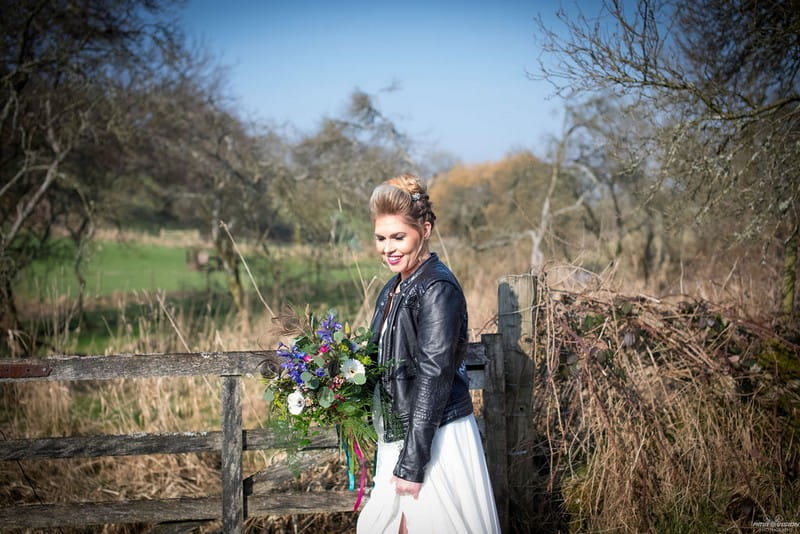Bride in leather jacket standing by gate in countryside