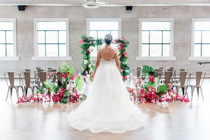Bride standing in front of ceremony backdrop and seating tropically styled with bougainvillea