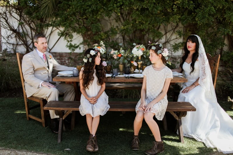 Bride, groom and flower girls sitting at rustic wedding table