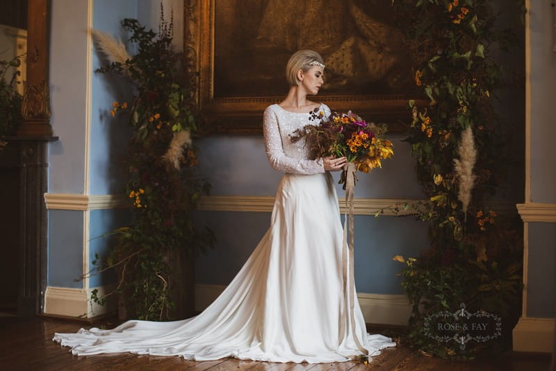 Bride in long sleeved dress holding autumnal bouquet