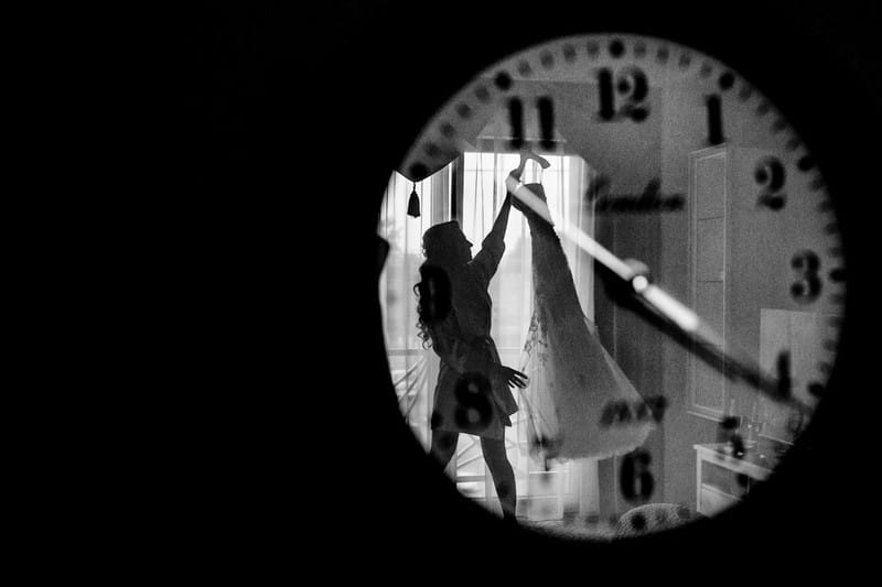 Reflection in clock of bride taking wedding dress down off rail - Picture by Sabina Mladin Photographer