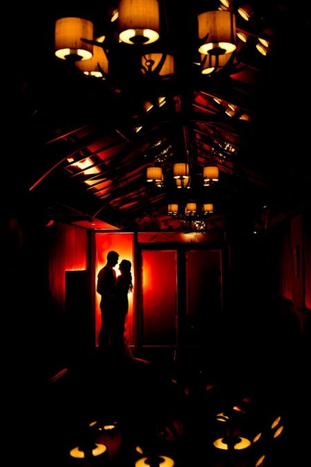 Silhouette of bride and groom at end of room lit with orange light from lamps - Picture by Matt Selby Photography