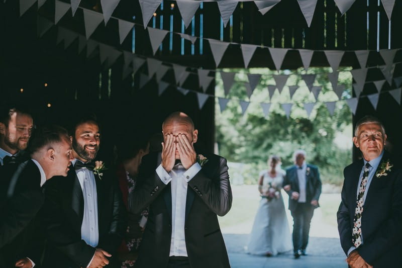 Groom with hands over his eyes to wipe away tears as bride walks down the aisle - Picture by Ross Talling Photography
