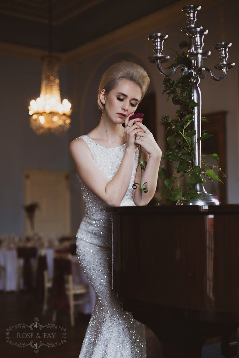 Bride standing holding rose next to piano