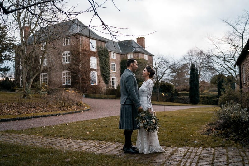 Bride and groom facing each other with Dewsall Court in background