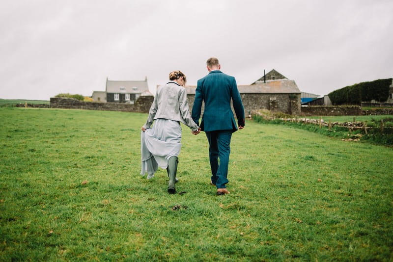 Bride and groom holding hands as they walk across farmland to wedding venue