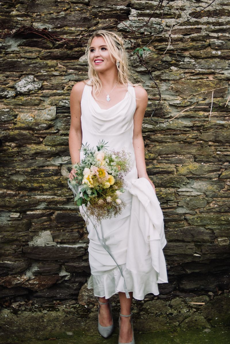 Bride holding bouquet as she stands against wall