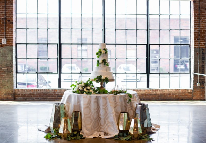 Wedding cake table dressed with foliage and gold lanterns