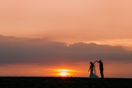 Bride twirling under groom's arm as sun sets in background - Picture by John Hope Photography