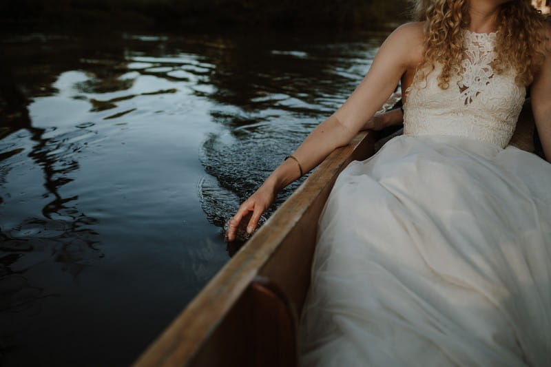 Bride sitting in boat with hand in the water - Picture by Caro Weiss Photography