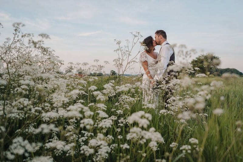 Bride and groom kissing in field of white flowers - Picture by Mr & Mrs