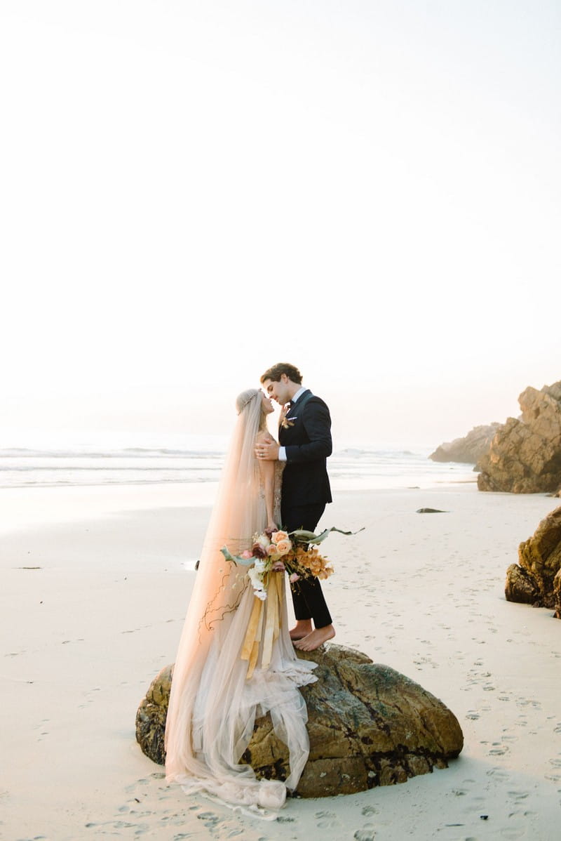 Bride and groom standing on rock on beach